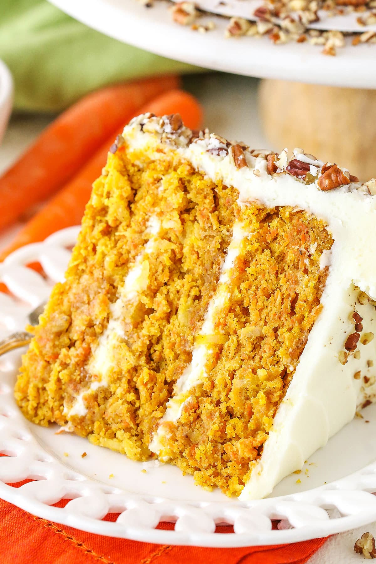 A slice of Carrot Cake on it's side next to a silver fork on a white plate