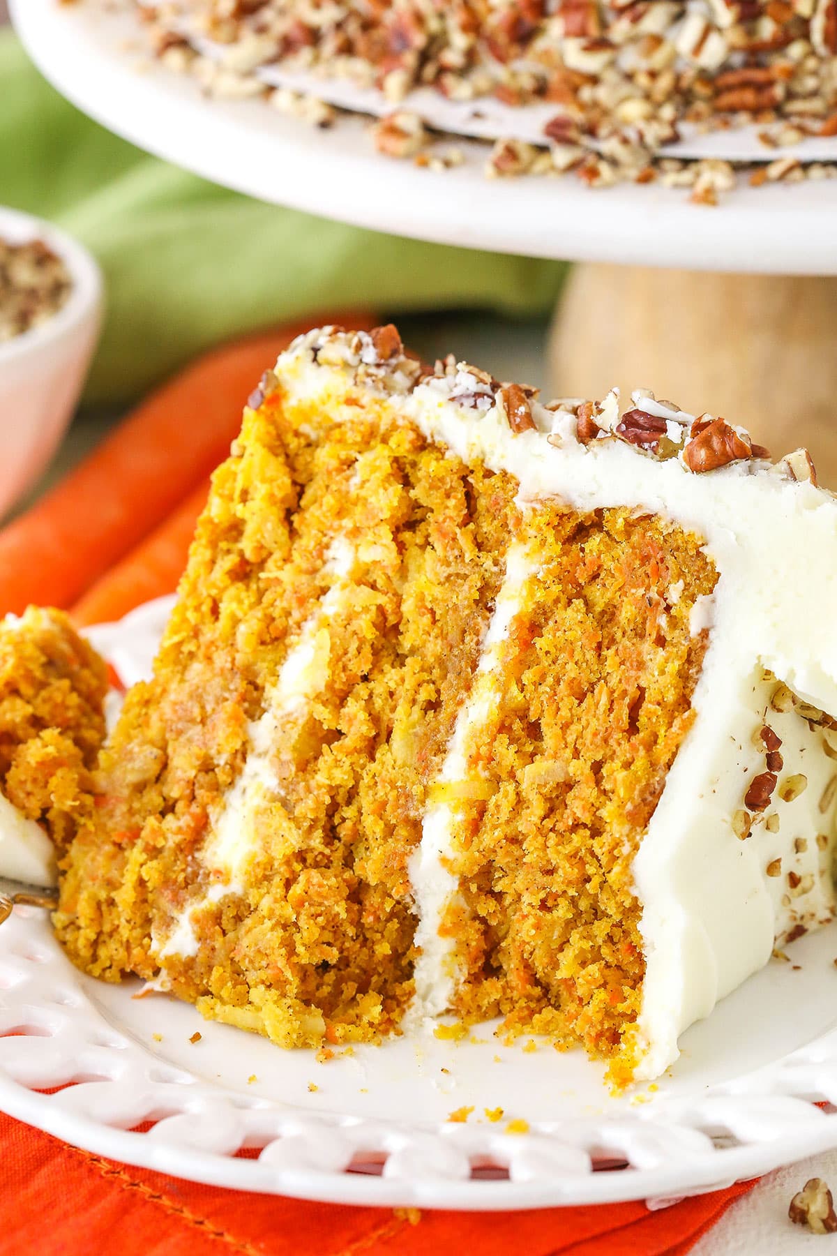 A slice of Carrot Cake on it's side with a bite removed next to a silver fork on a white plate