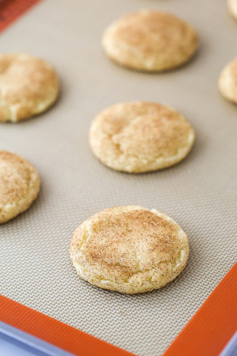 Snickerdoodles on a baking sheet lined with a baking mat.