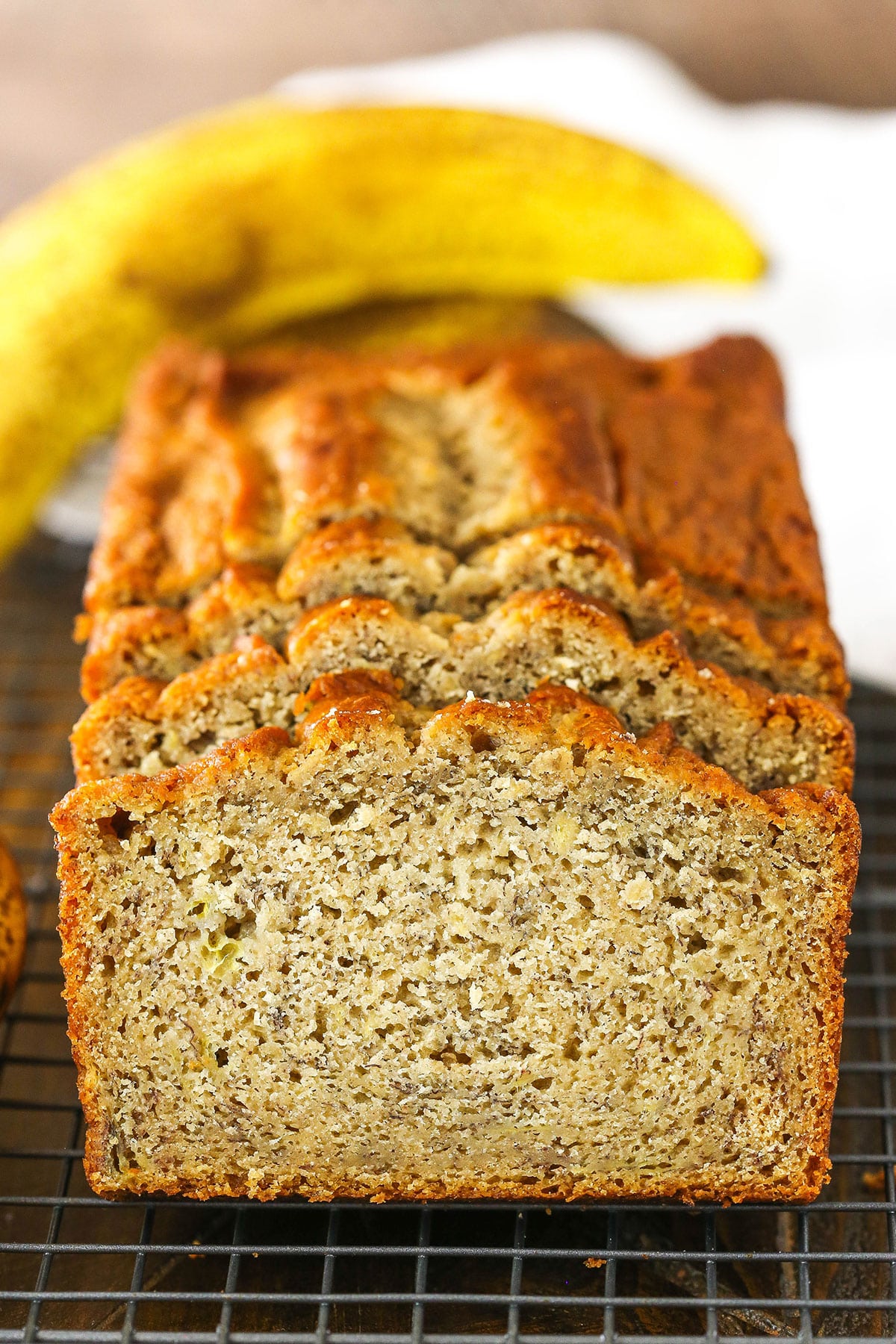 Side view of three Banana Bread slices leaning against the remaining banana bread loaf on a cooling rack