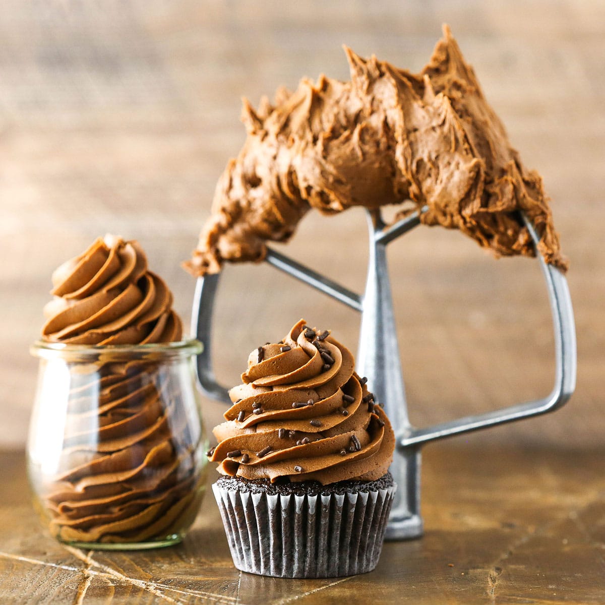 Fudgy Chocolate Buttercream Frosting piped onto a chocolate cupcake, into a clear glass jar and on a beater blade