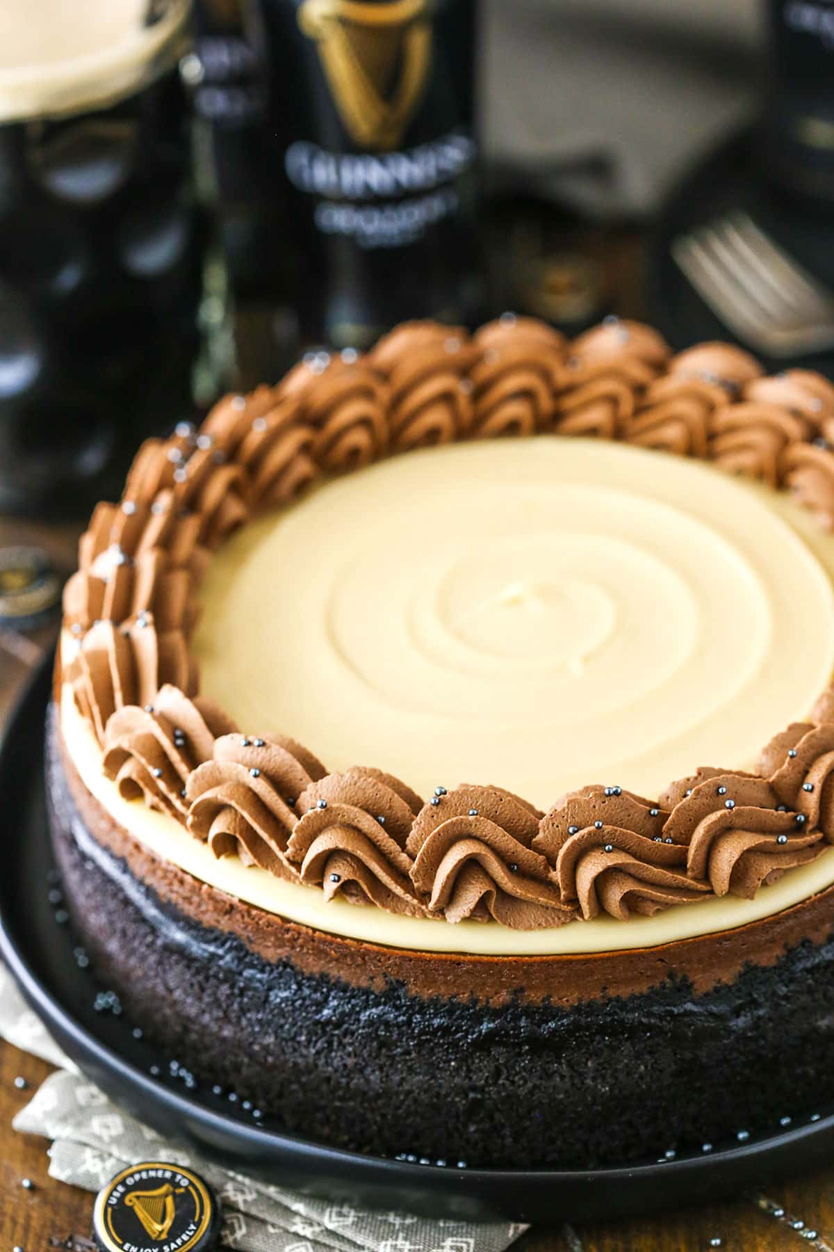 This Guinness Chocolate Cheesecake is made with a chocolate filling, Oreo cookie crust, Baileys ganache topping and Guinness chocolate whipped cream! It's so smooth, creamy and such a decadent cheesecake recipe! A full Guinness Chocolate Cheesecake on a black plate