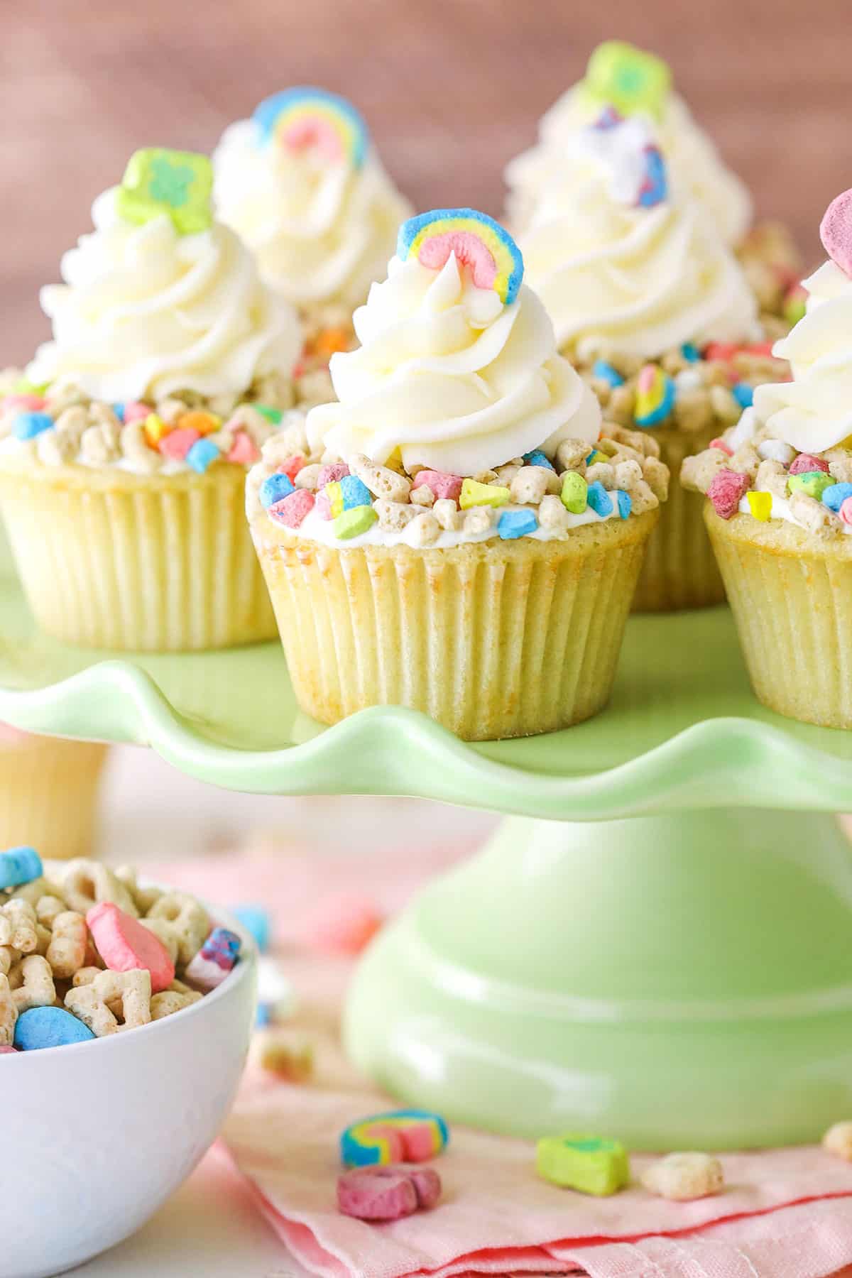 These Lucky Charms Cupcakes are made with cereal milk cupcakes, Lucky Charms marshmallow filling, Lucky Charms crumbled on top and a light swirl of cereal milk frosting! They take me back to being a kid and they are SO tasty! Lucky Charms Cupcakes on a light green cake stand