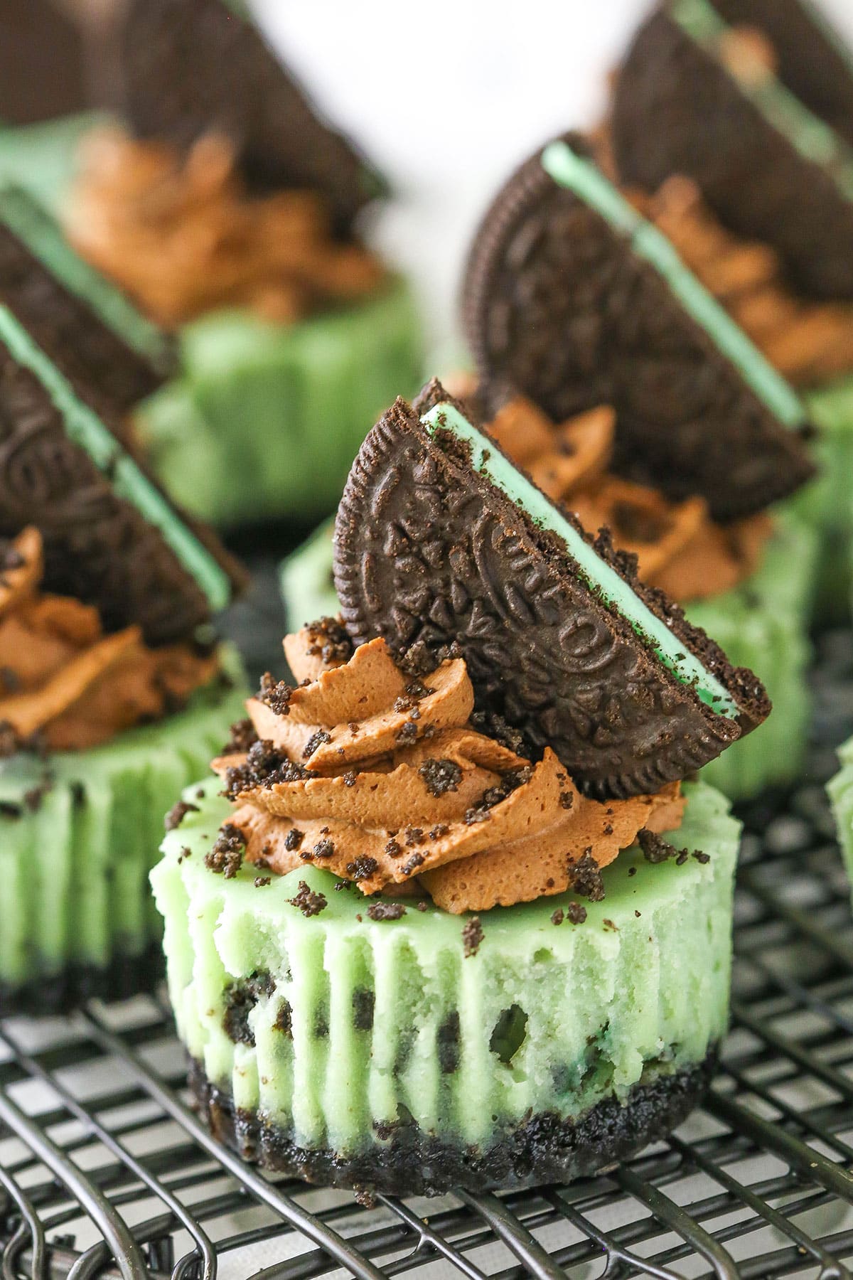These sharable mint chocolate Oreo mini cheesecakes are made up of Oreo crust, minty, Oreo-y cheesecake filling, and chocolate whipped cream. Side view of Mini Mint Chocolate Oreo Cheesecakes on a gray metal stand