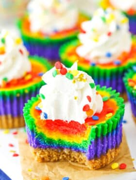 A Mini Rainbow Cheesecake with a bite removed on a white serving tray