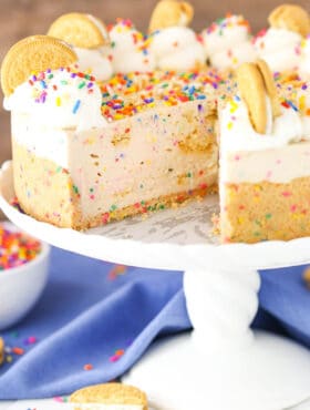 No-Bake Funfetti Oreo Birthday Cake Cheesecake with a slice removed on a white cake stand