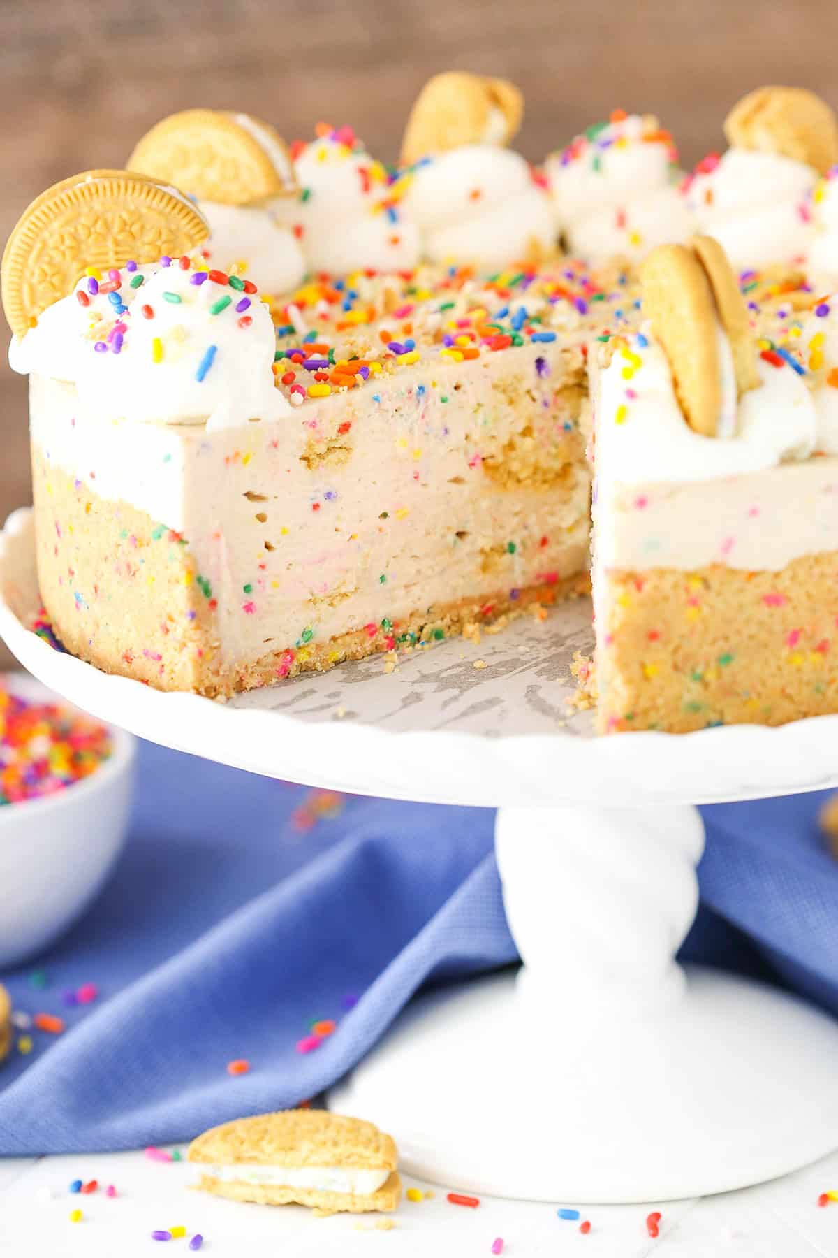 No-Bake Funfetti Oreo Birthday Cake Cheesecake with a slice removed on a white cake stand