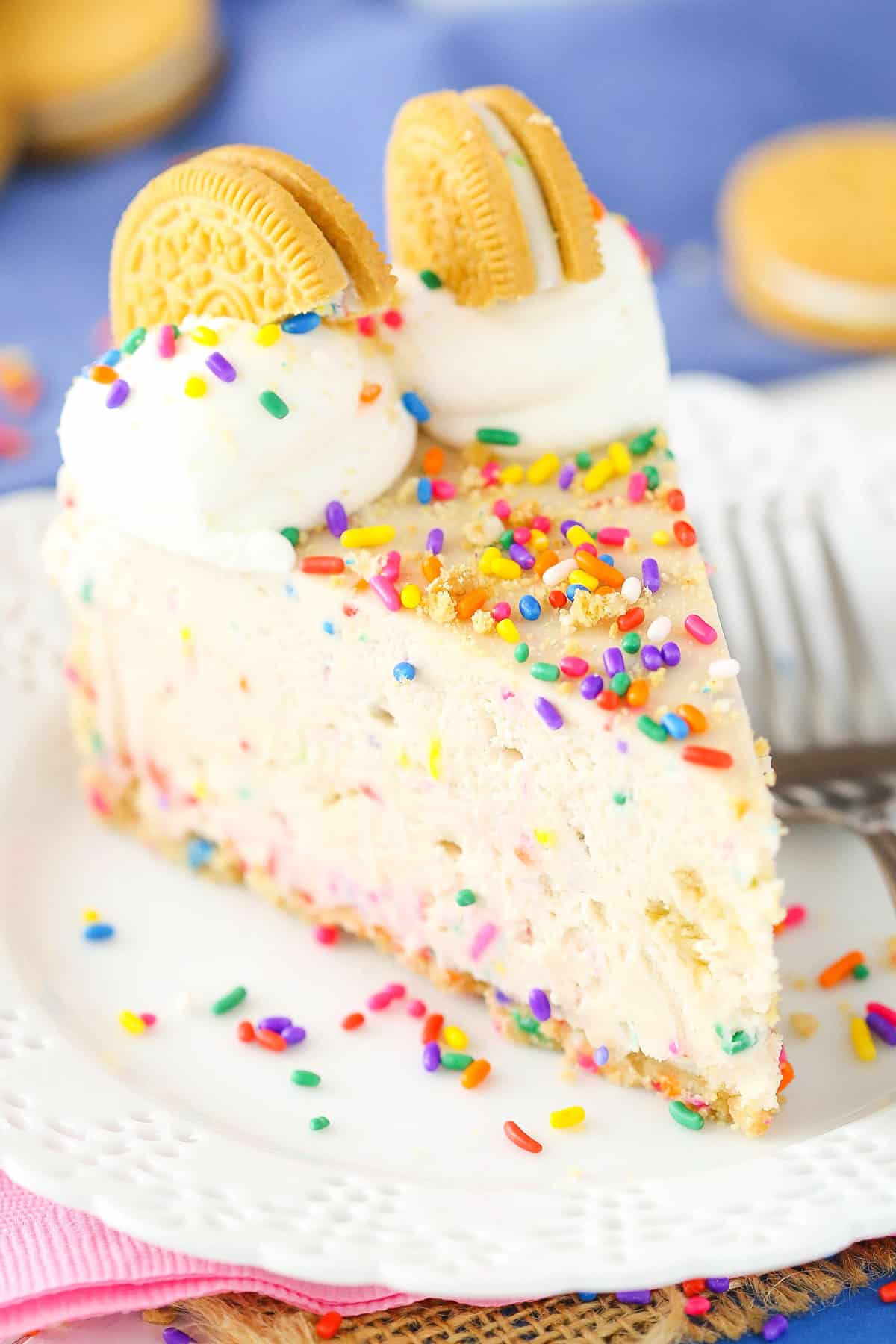 A slice of No-Bake Funfetti Oreo Birthday Cake Cheesecake next to a silver fork on a white plate