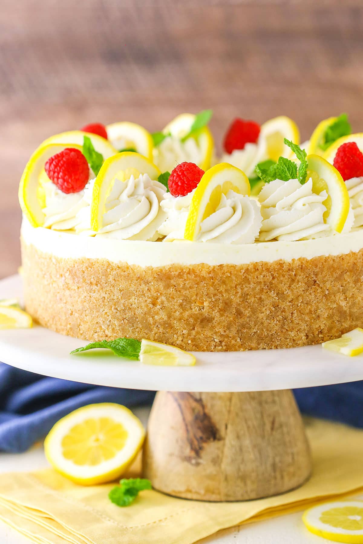 Side view of the whole No Bake Lemon Cheesecake on a white cake stand with a wooden base