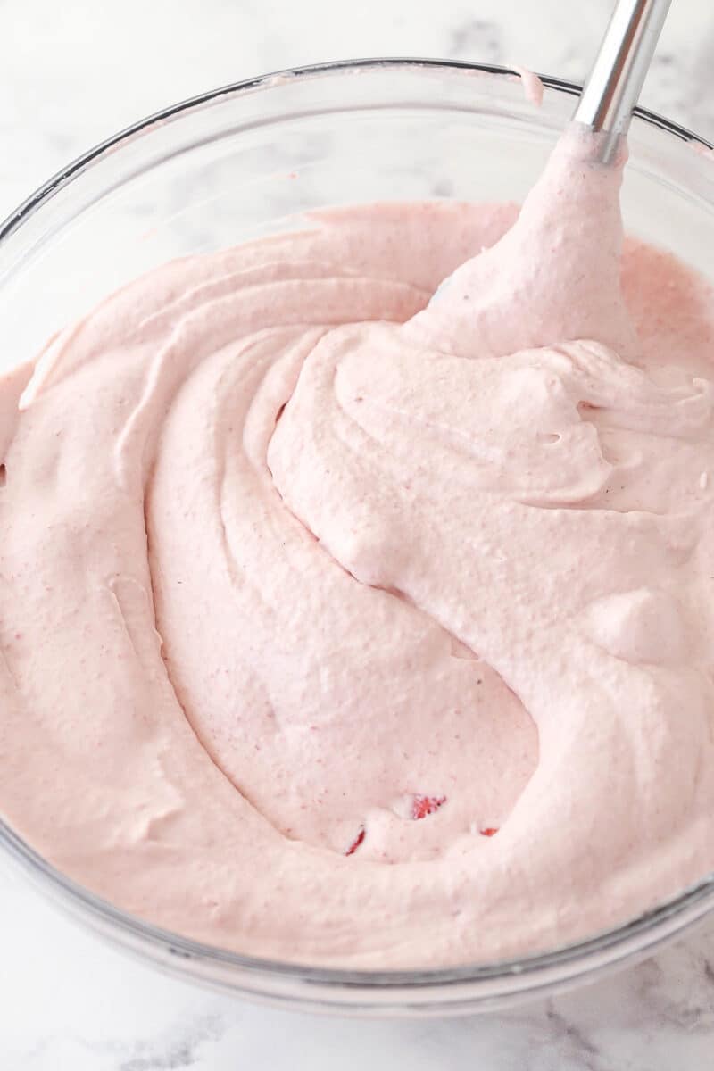 whipped cream folded into strawberry mixture in glass bowl