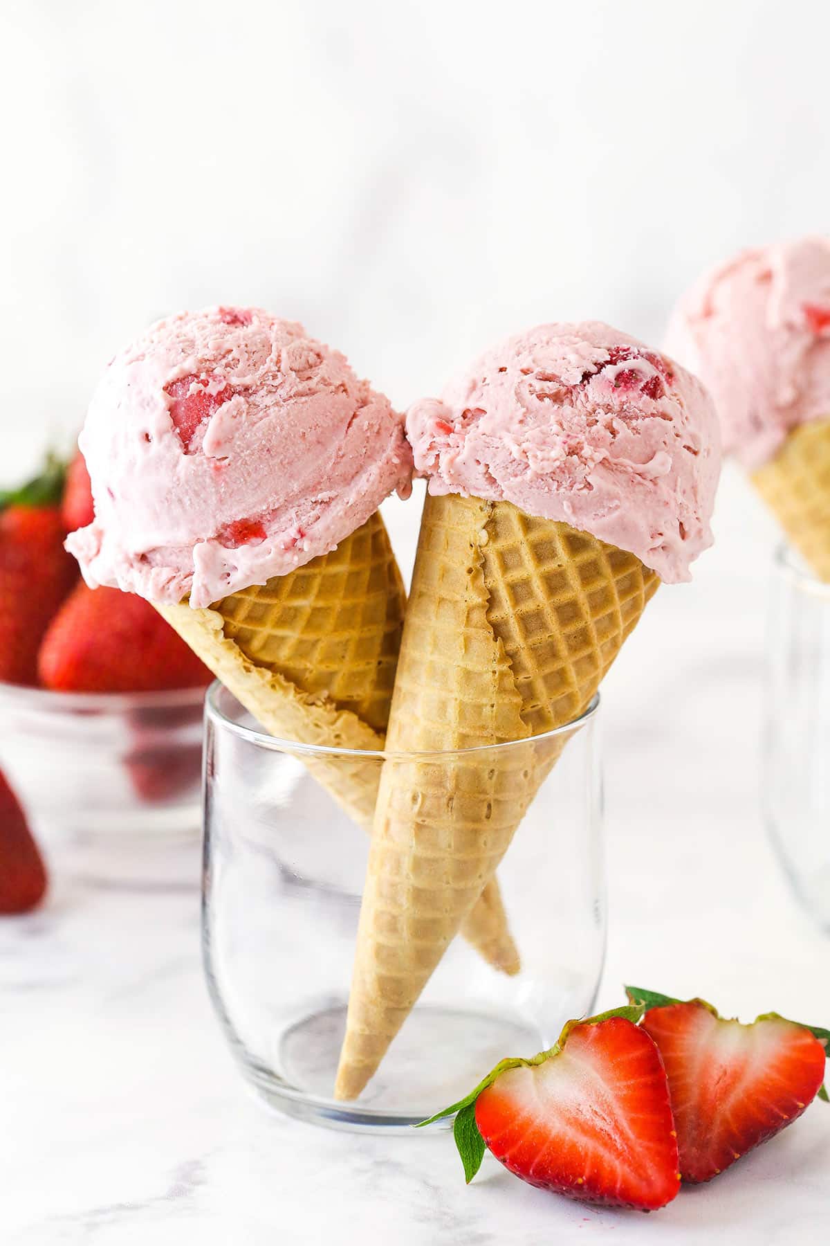 two ice cream cones with scoops of strawberry ice cream in them, propped up in glass cup