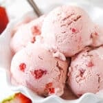 scoops of strawberry ice cream in white ruffled dish with a spoon