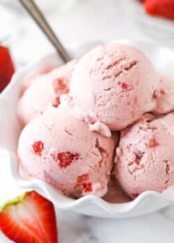 scoops of strawberry ice cream in white ruffled dish with a spoon