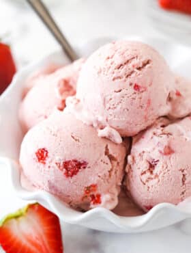scoops of strawberry ice cream in white ruffled dish with a spoon