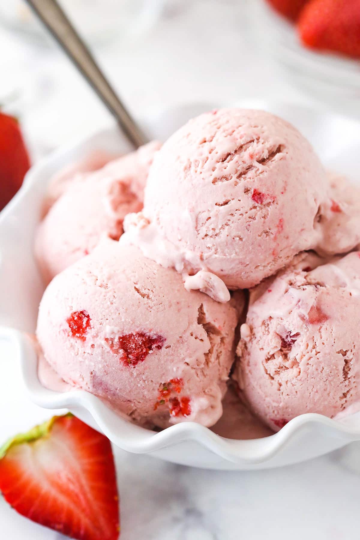 scoops of strawberry ice cream in white ruffled dish with a spoon