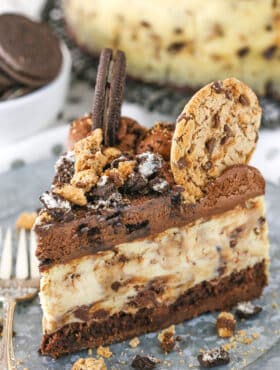 A slice of Oreo Brookie Cheesecake next to a silver fork on a gray plate