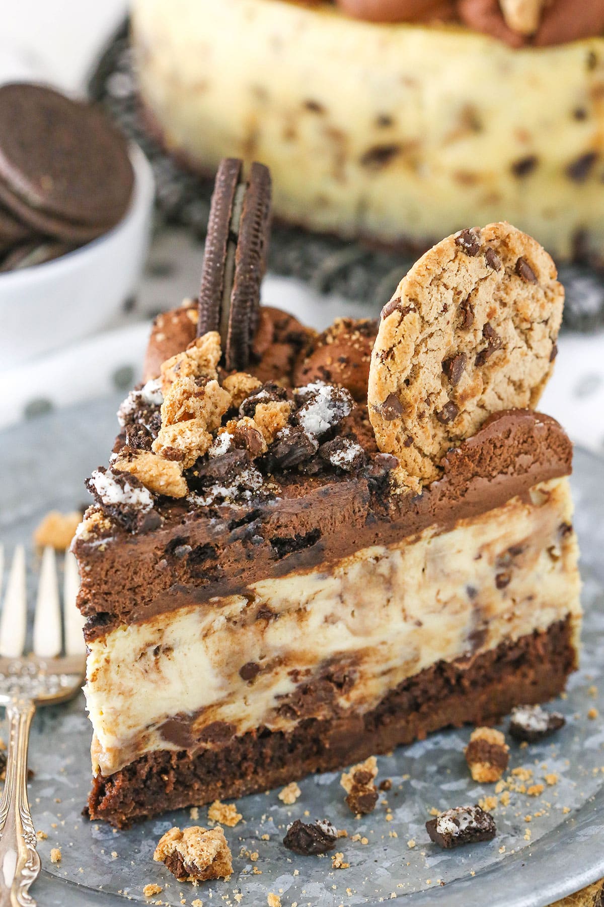 A slice of Oreo Brookie Cheesecake next to a silver fork on a gray plate