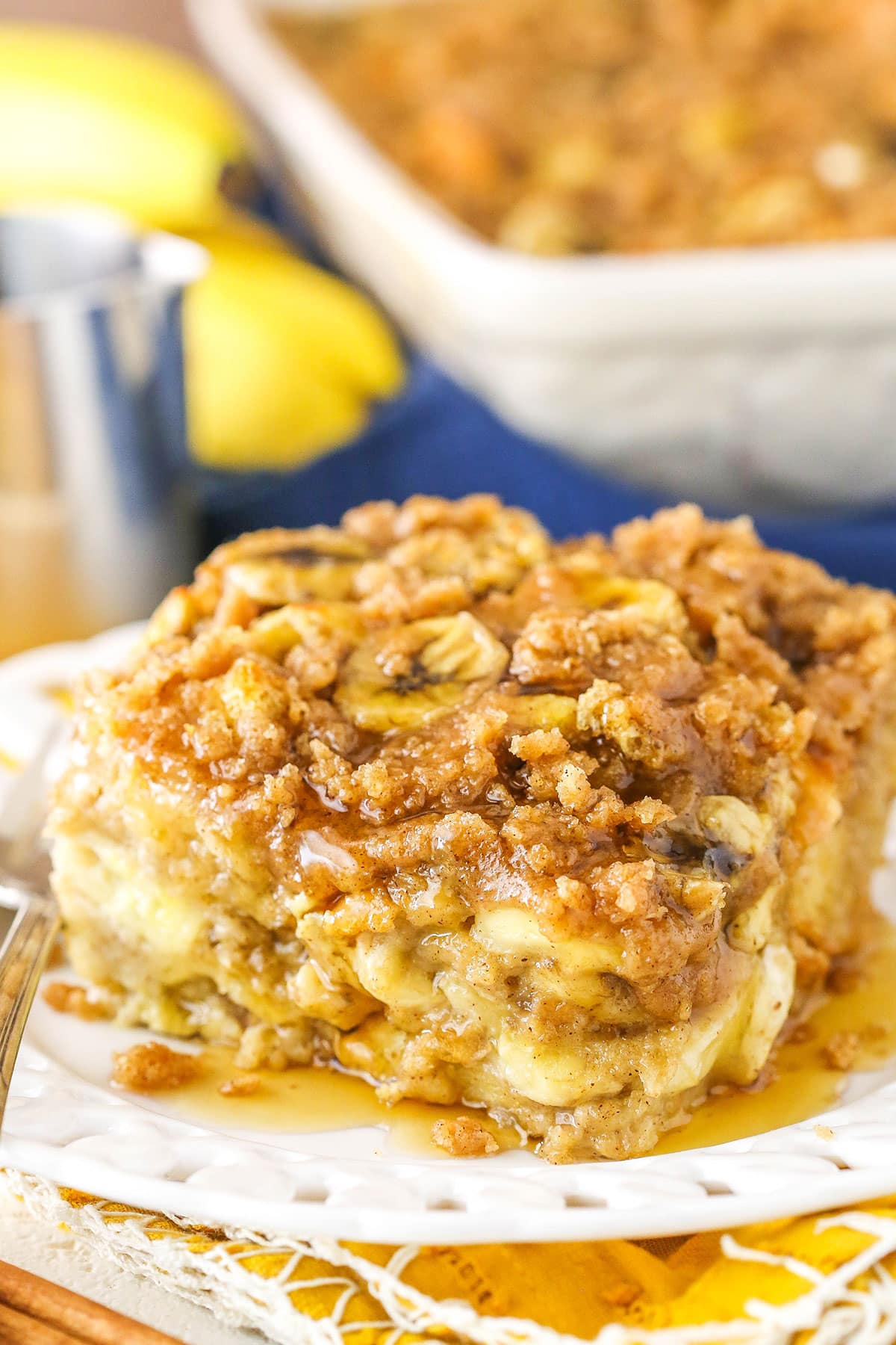 A square serving of Overnight Baked Banana French Toast Casserole next to a silver fork on a white plate