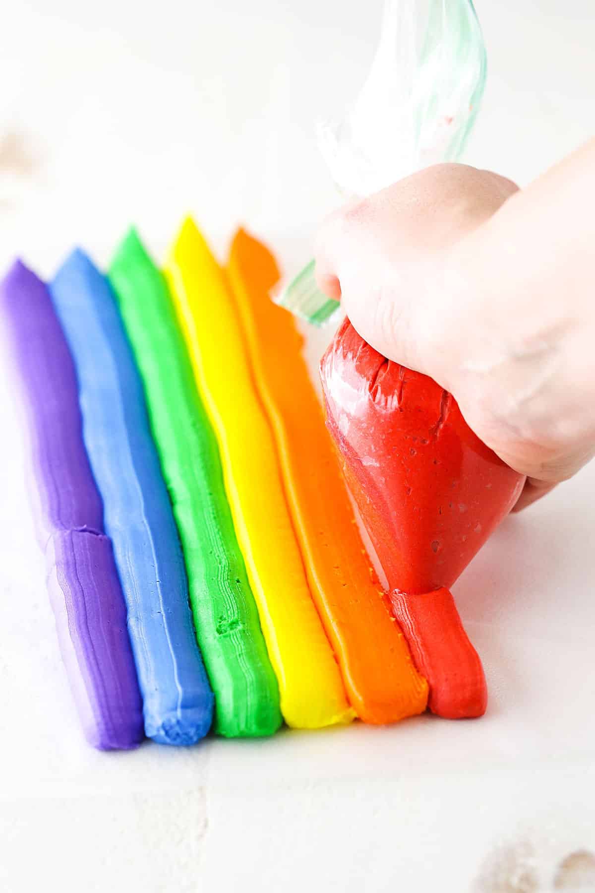 A step in making Rainbow Swirl Cake showing piping rows of different colored frosting using a piping bag