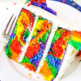 A slice of Rainbow Swirl Cake next to a silver fork on a white plate