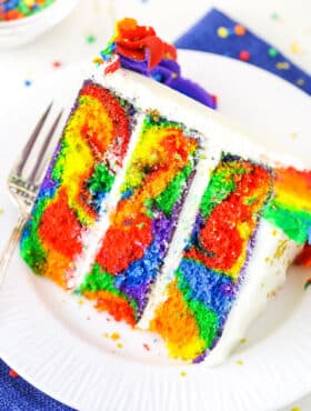 A slice of Rainbow Swirl Cake next to a silver fork on a white plate