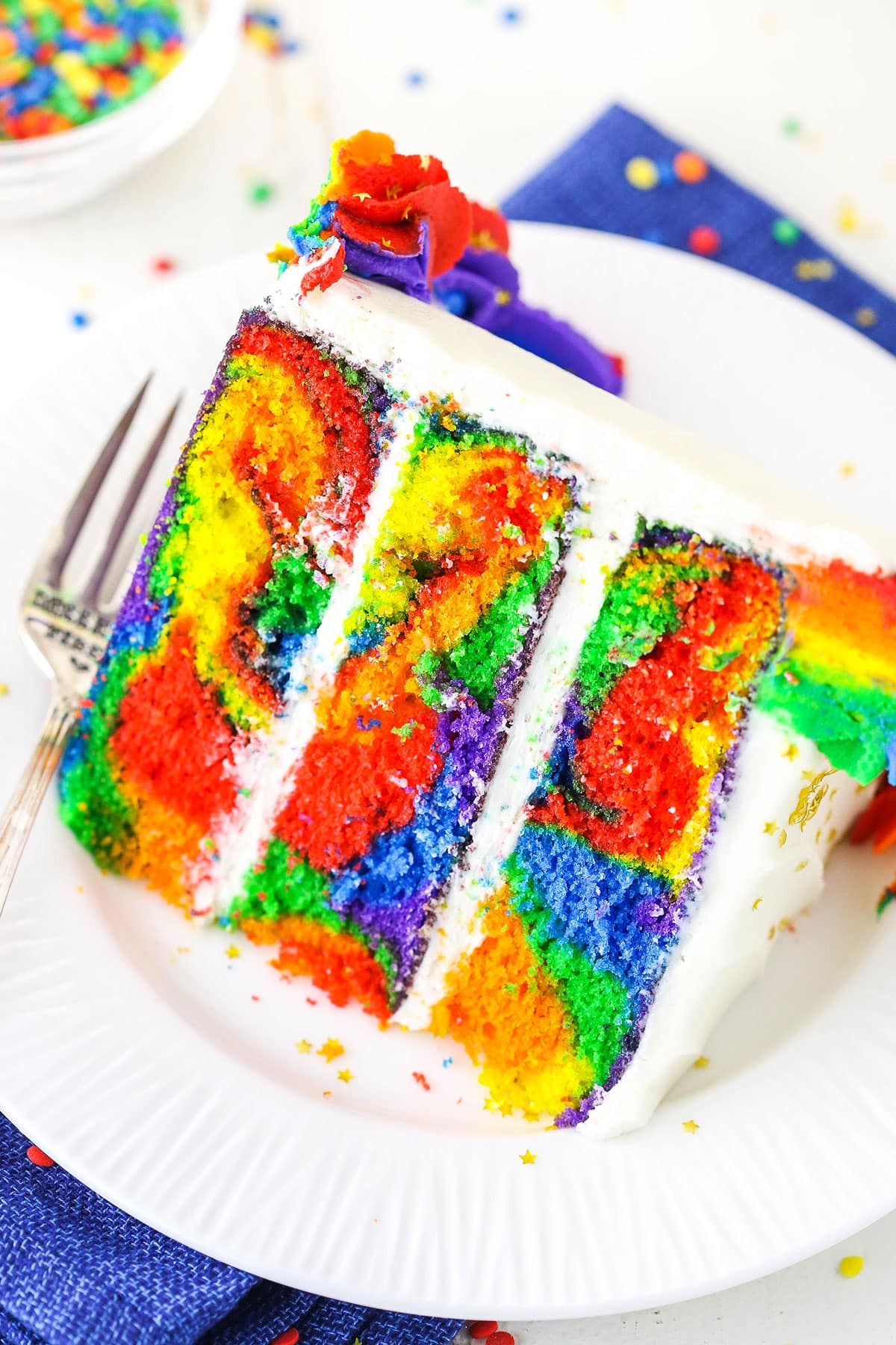 A slice of Rainbow Swirl Cake next to a silver fork on a white plate