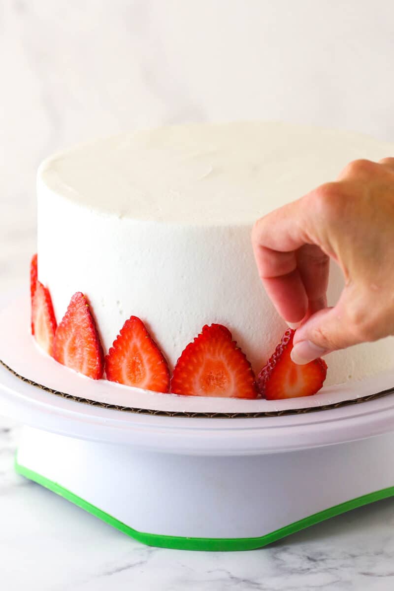 Decorating strawberry ice cream cake with fresh strawberry slices.