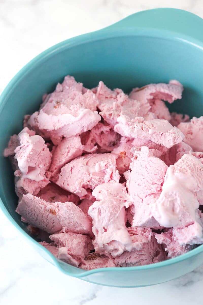 Strawberry ice cream scooped into a large mixing bowl to soften.