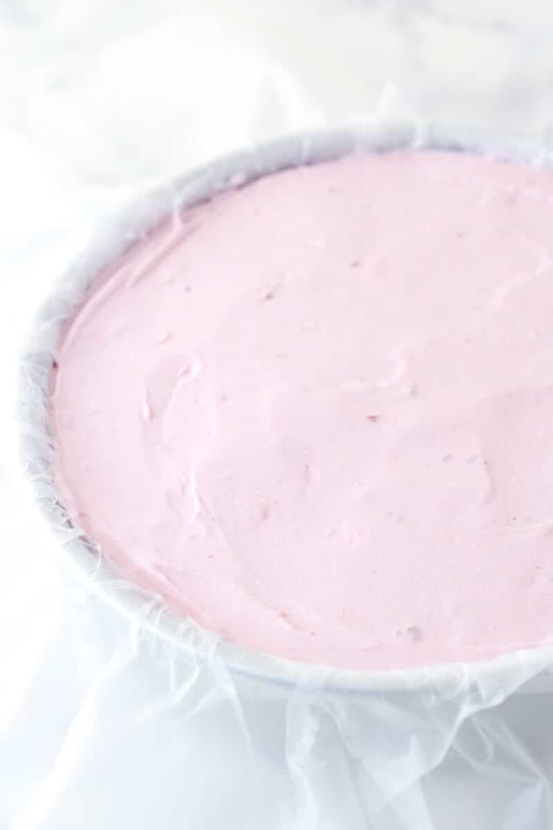 Spreading softened strawberry ice cream into a cake pan lined with clear wrap.