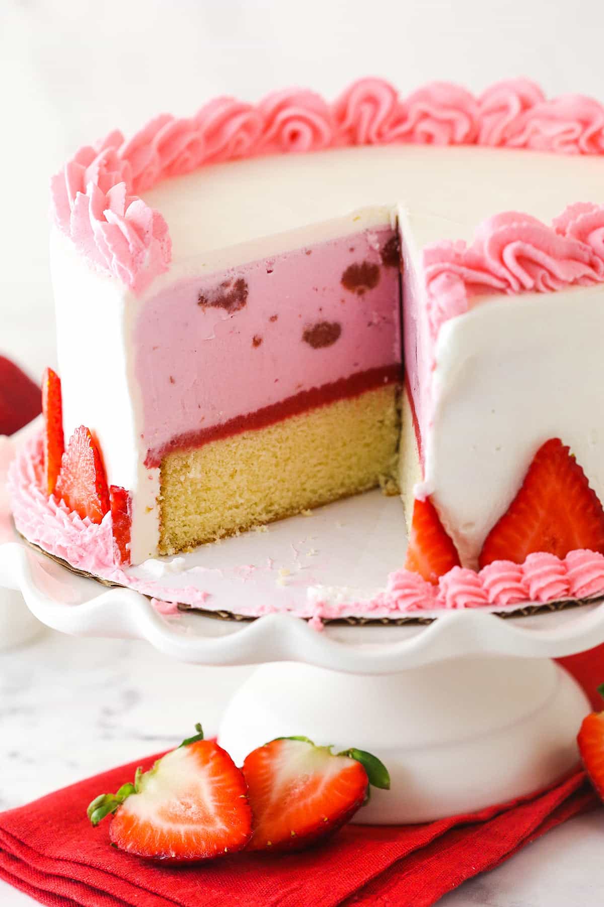 Strawberry ice cream cake on a cake stand with a couple of slices taken out of it.