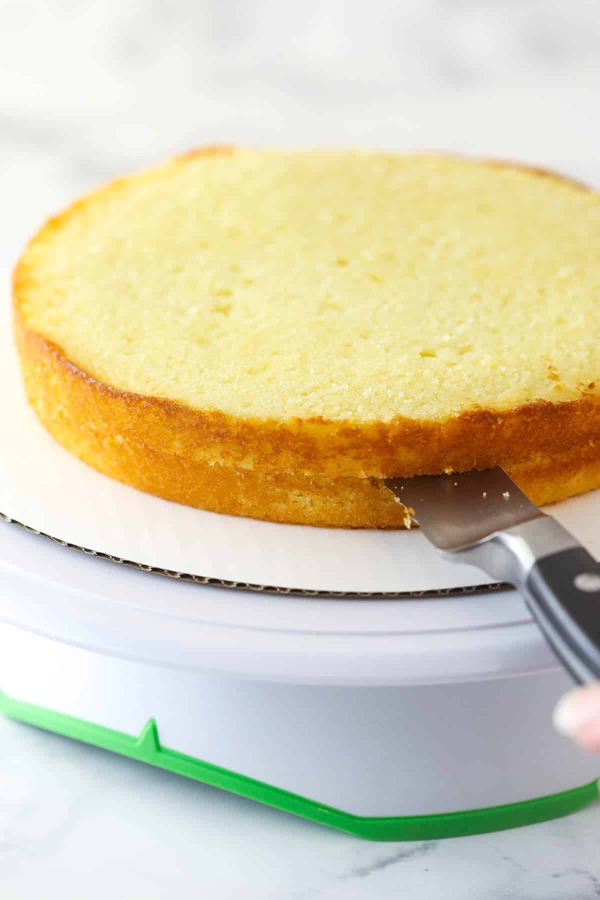 Cutting a layer of lemon cake in half horizontally to make 2 layers.