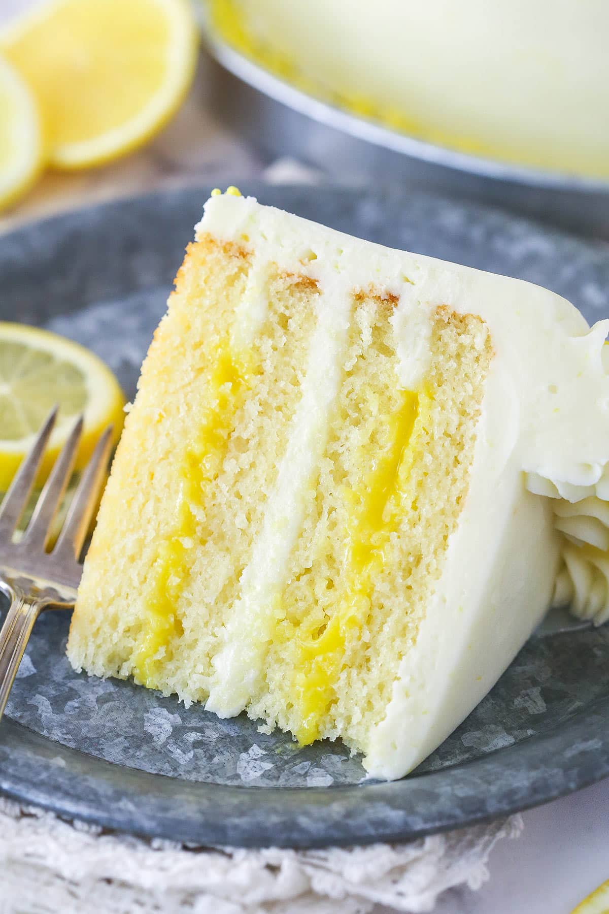 Lemon curd cake is made of 4 layers of tender, sweet, tangy lemon cake filled with lemon curd and frosted with smooth lemon buttercream. A slice of lemon curd cake on a plate.