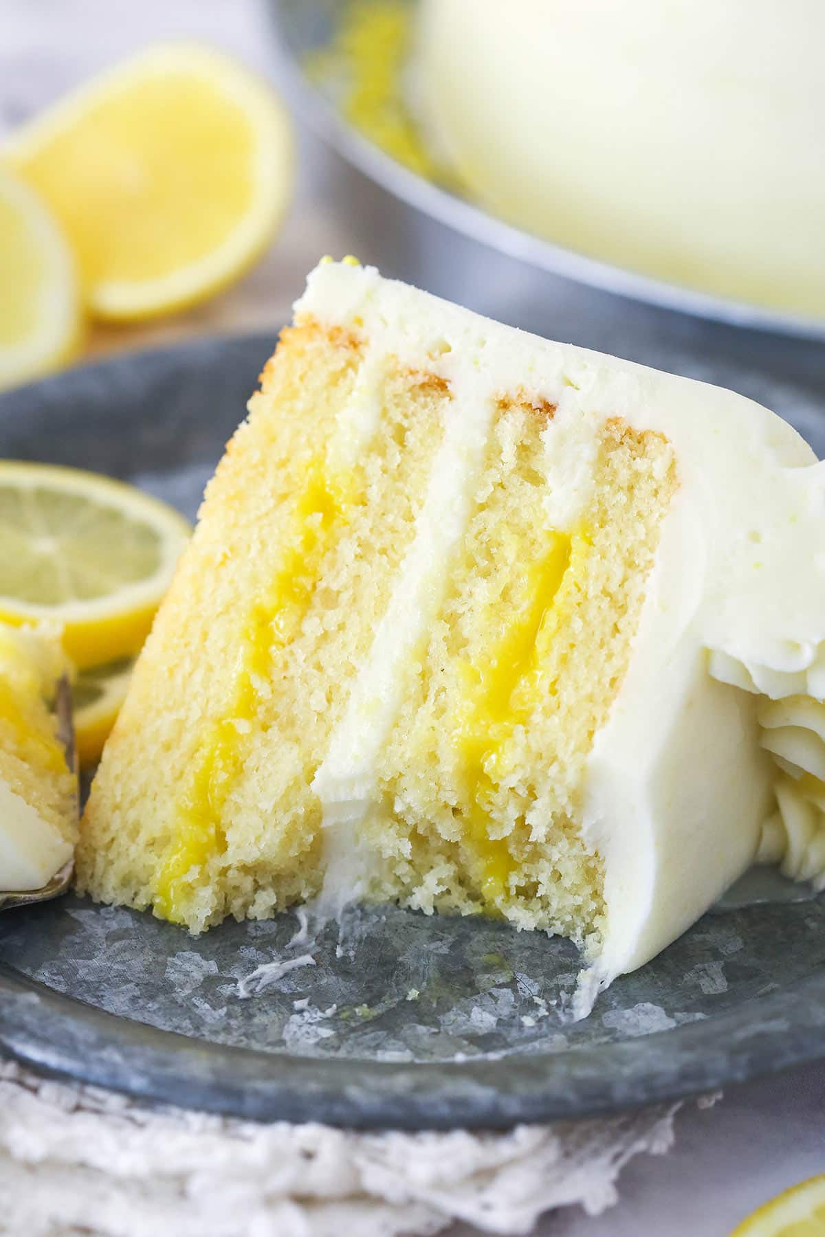 A slice of lemon curd cake on a plate with a bite taken out of it.