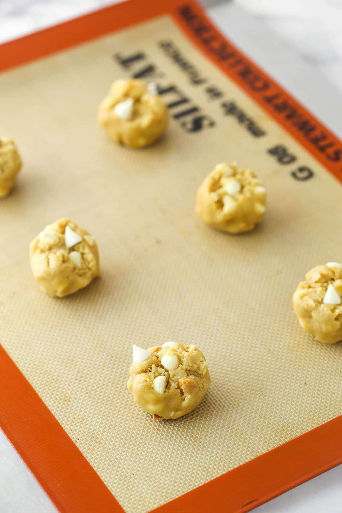 White chocolate macadamia nut cookie dough balls arranged on a silicone baking mat.