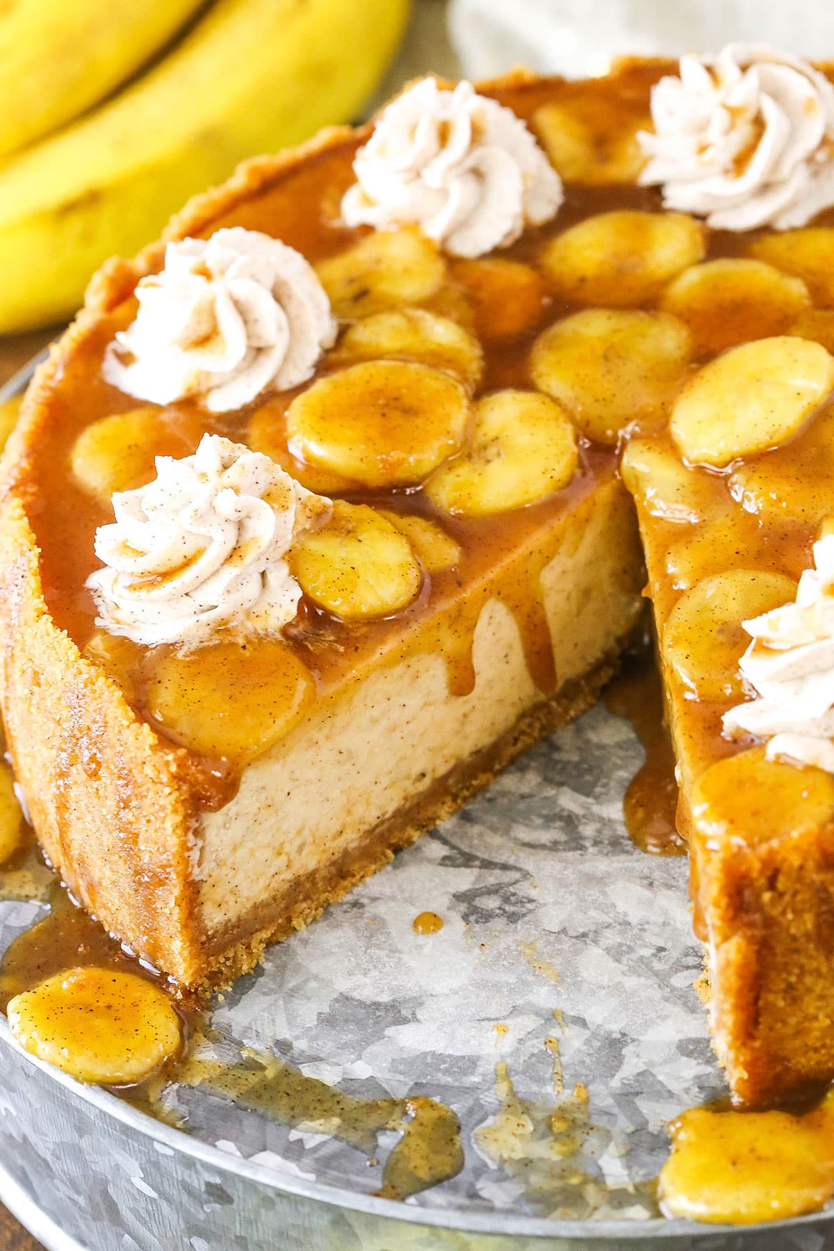 A Bananas Foster Cheesecake with a slice removed on a metal cake stand