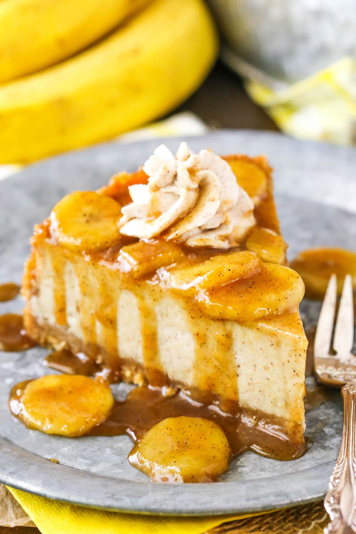 A slice of Bananas Foster Cheesecake next to a silver fork on a gray plate