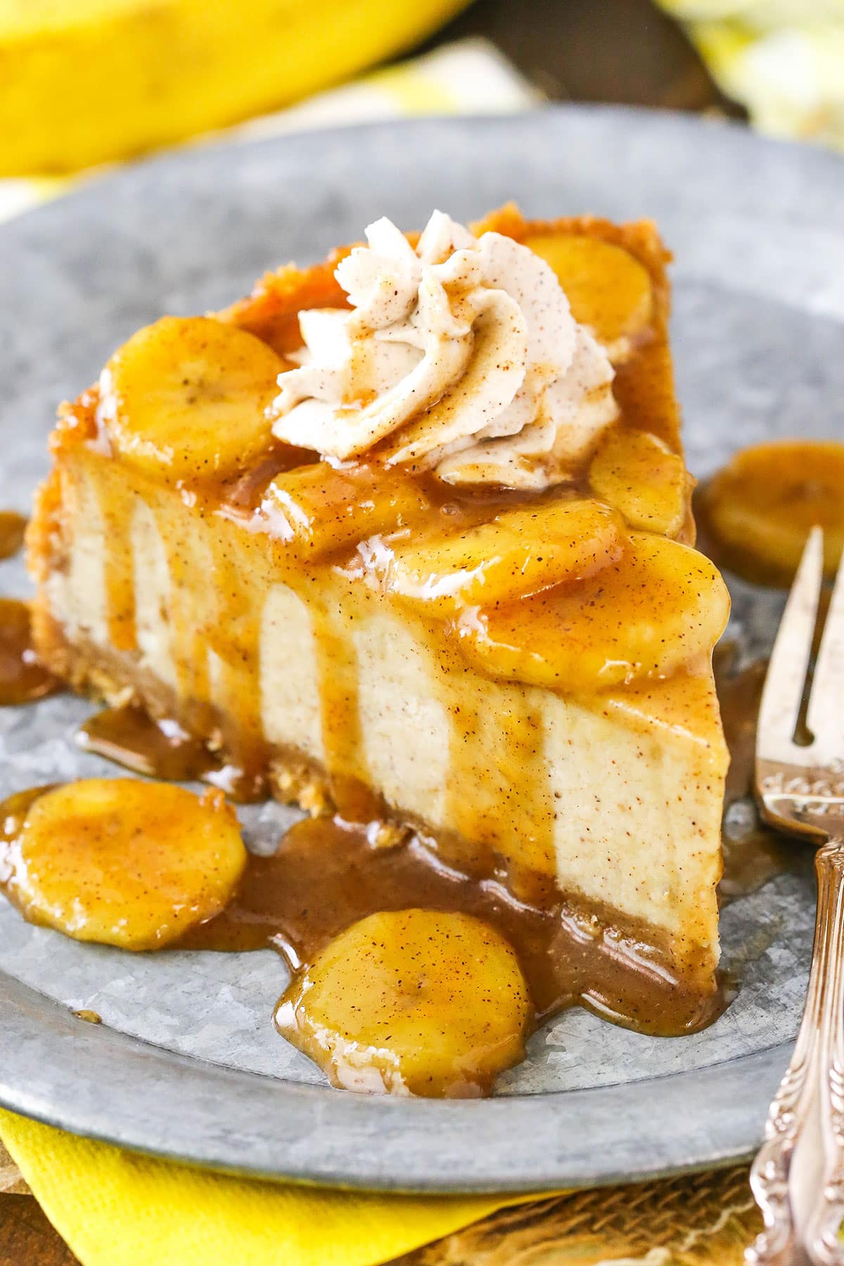 A slice of Bananas Foster Cheesecake next to a silver fork on a gray plate