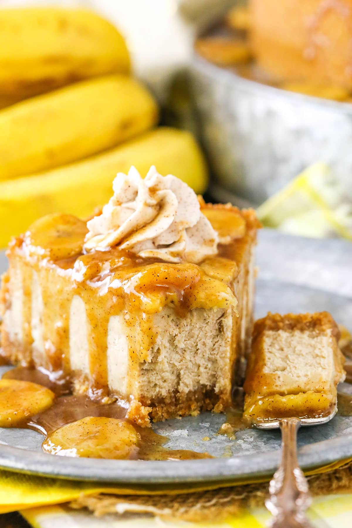 A slice of Bananas Foster Cheesecake with a bite removed next to a silver fork on a gray plate