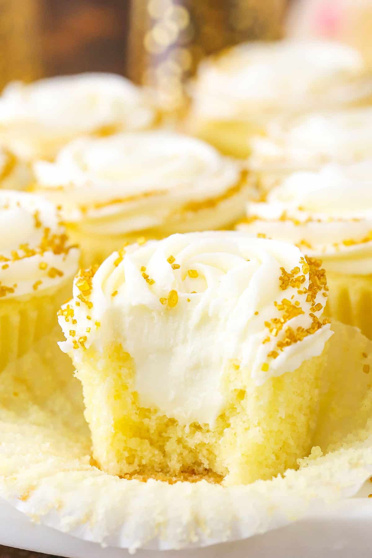 These Champagne Cupcakes are filled with white chocolate champagne truffle filling and topped with champagne frosting! They are moist, light and FULL of champagne flavor! Perfect for a New Year's Eve party or any celebration! Champagne Cupcake With Truffle Filling with a bite removed