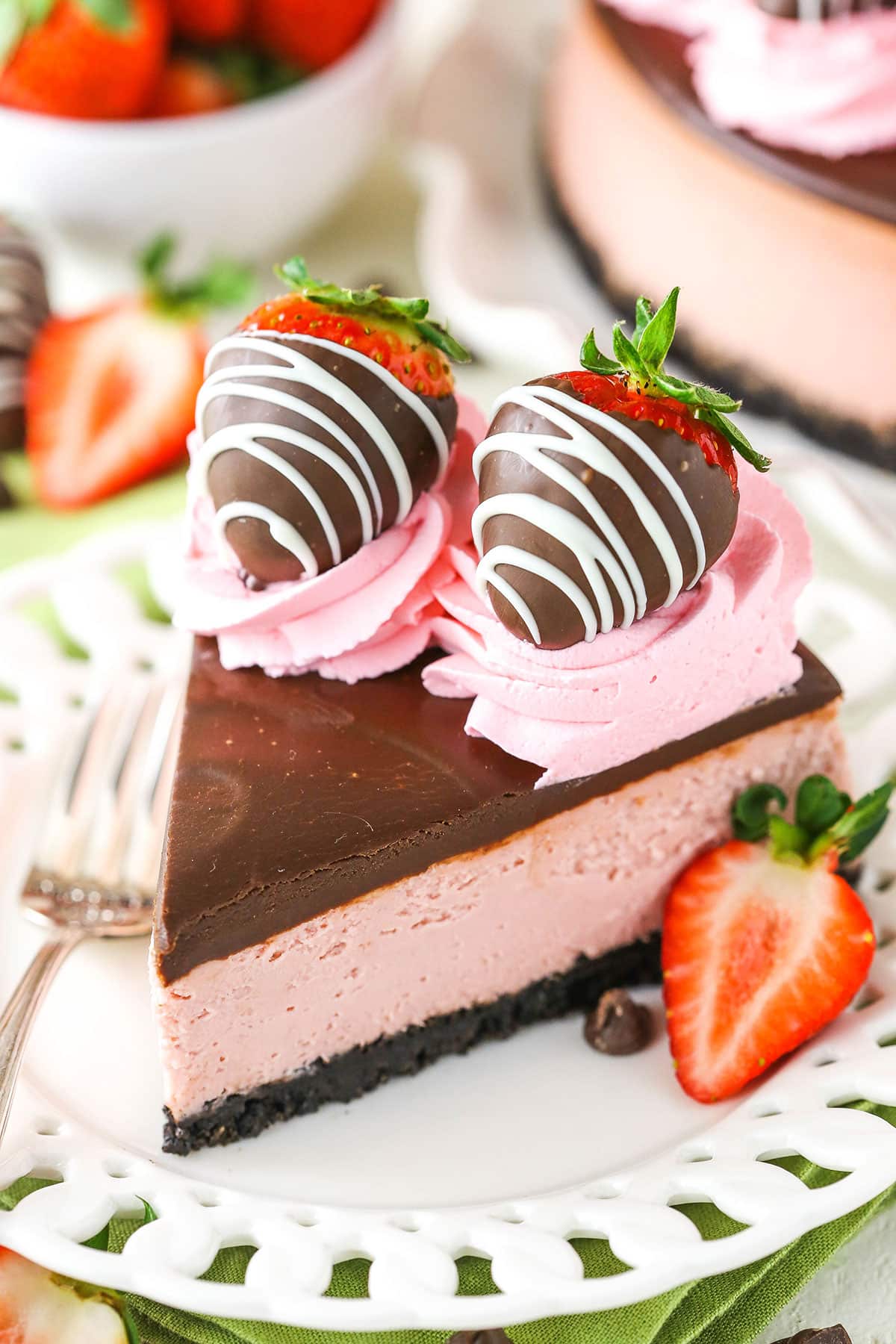 A slice of Chocolate Covered Strawberry Cheesecake next to a silver fork on a white plate