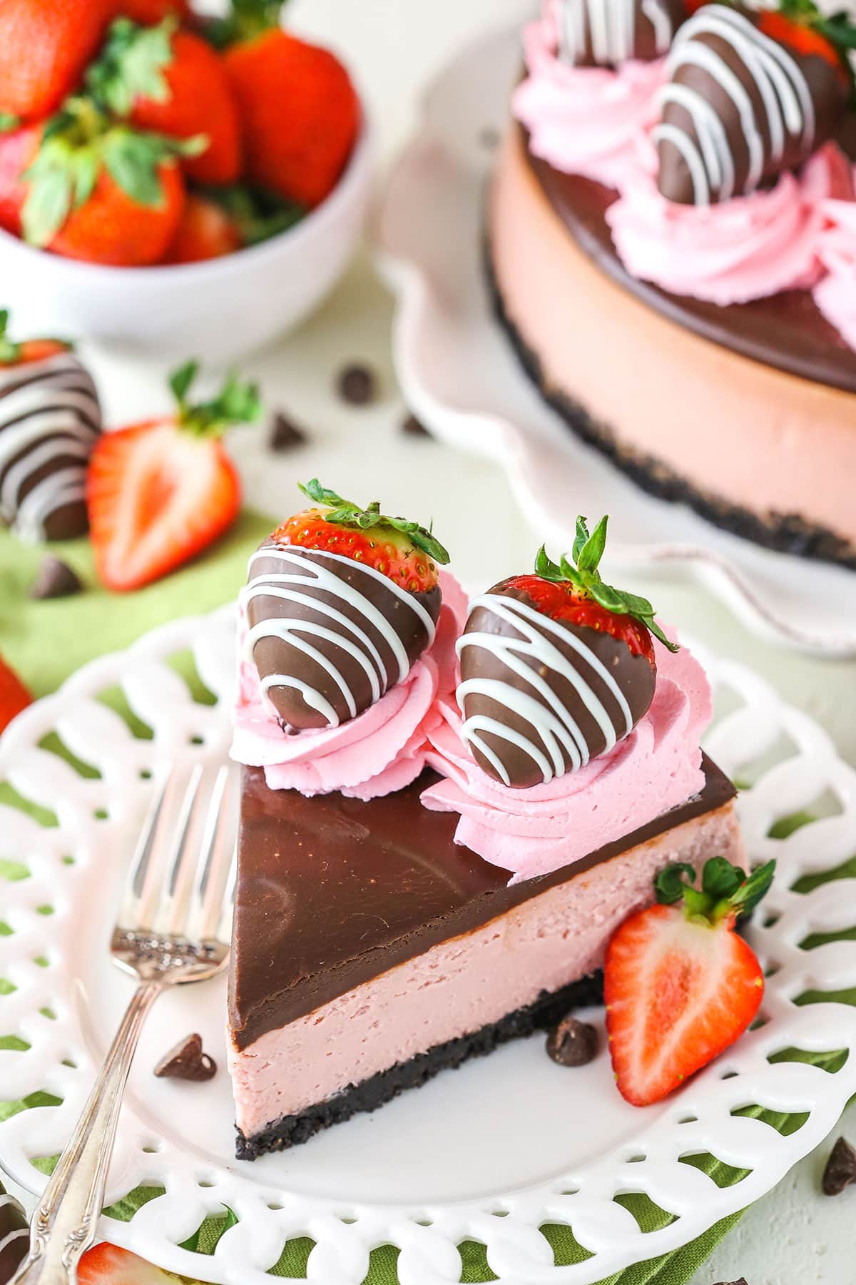 A slice of Chocolate Covered Strawberry Cheesecake next to a silver fork on a white plate