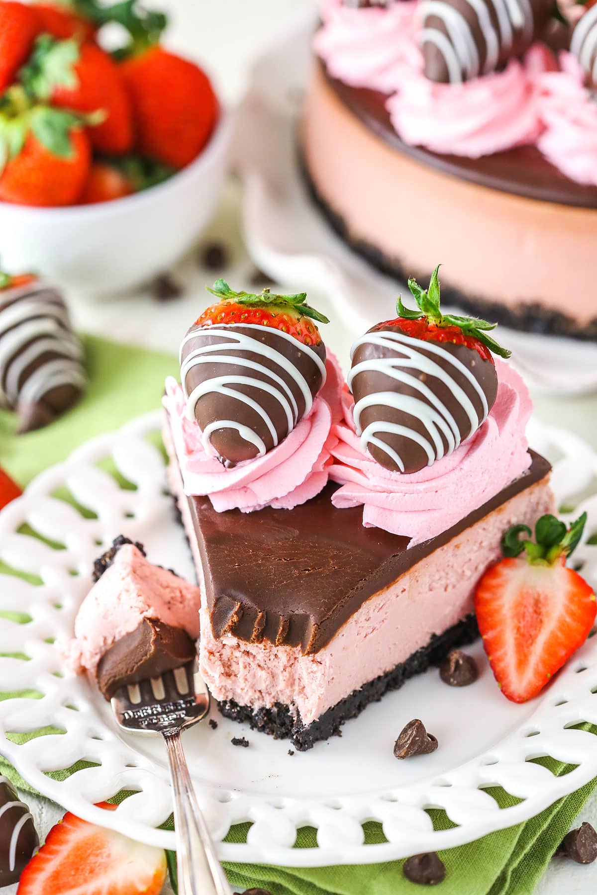 A slice of Chocolate Covered Strawberry Cheesecake with a bite removed next to a silver fork on a white plate
