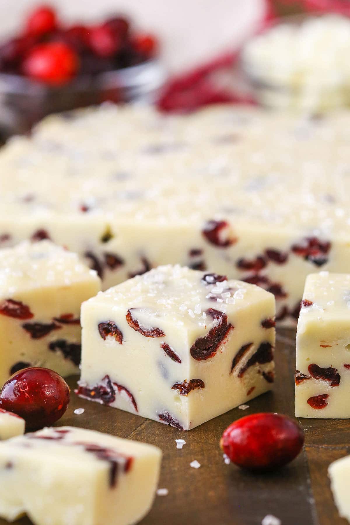 This White Chocolate Cranberry Fudge is made with sweetened condensed milk and dried cranberries! With beautiful Christmas colors, this super easy and quick dessert is a great treat for the busy holiday season! White Chocolate Cranberry Fudge cubes spread over a wooden table
