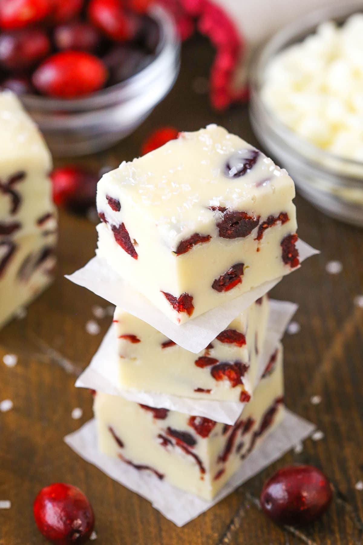 This White Chocolate Cranberry Fudge is made with sweetened condensed milk and dried cranberries! With beautiful Christmas colors, this super easy and quick dessert is a great treat for the busy holiday season! Three White Chocolate Cranberry Fudge cubes stacked on a wooden table