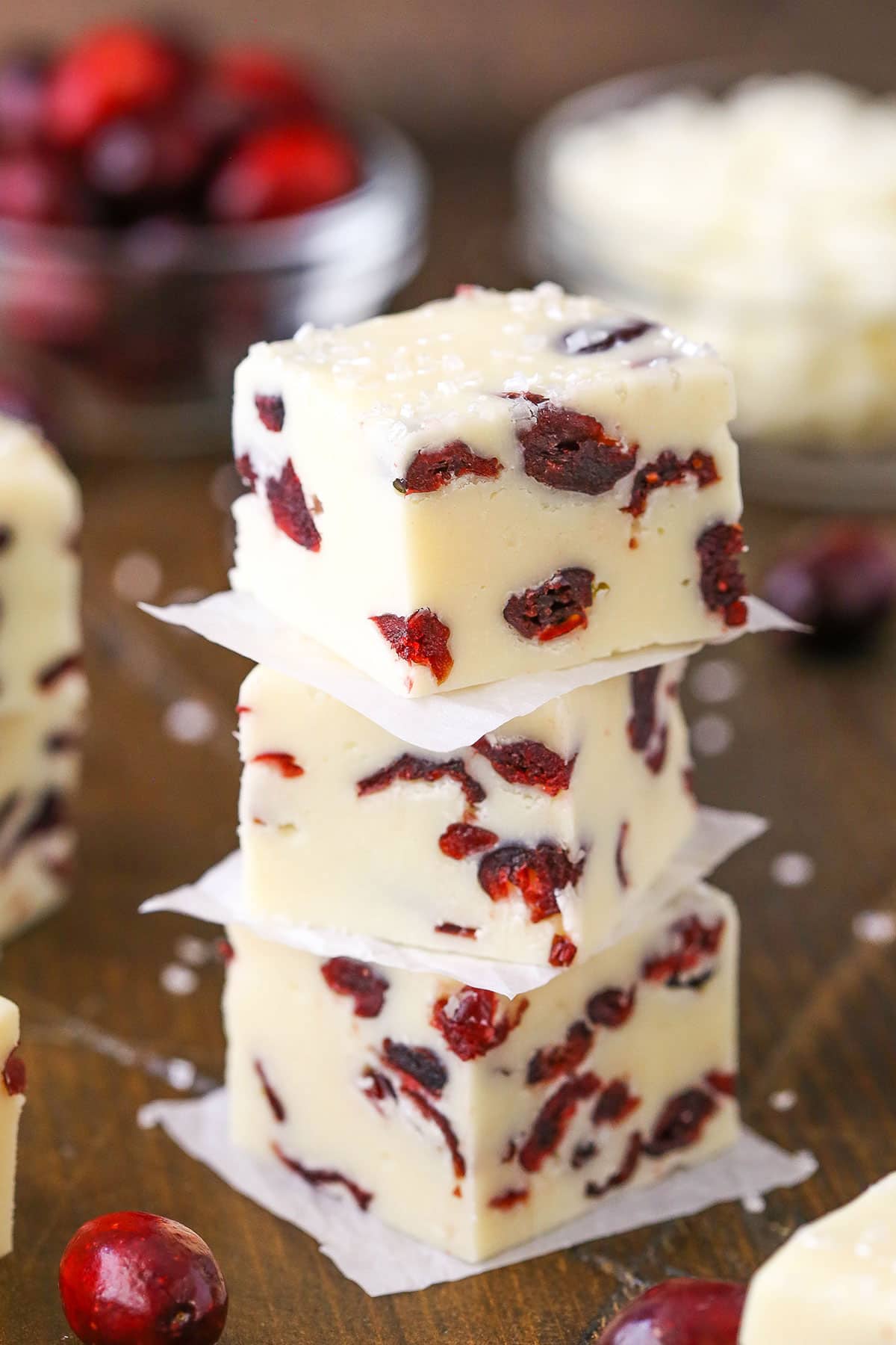 This White Chocolate Cranberry Fudge is made with sweetened condensed milk and dried cranberries! With beautiful Christmas colors, this super easy and quick dessert is a great treat for the busy holiday season! Three White Chocolate Cranberry Fudge cubes stacked on a wooden table