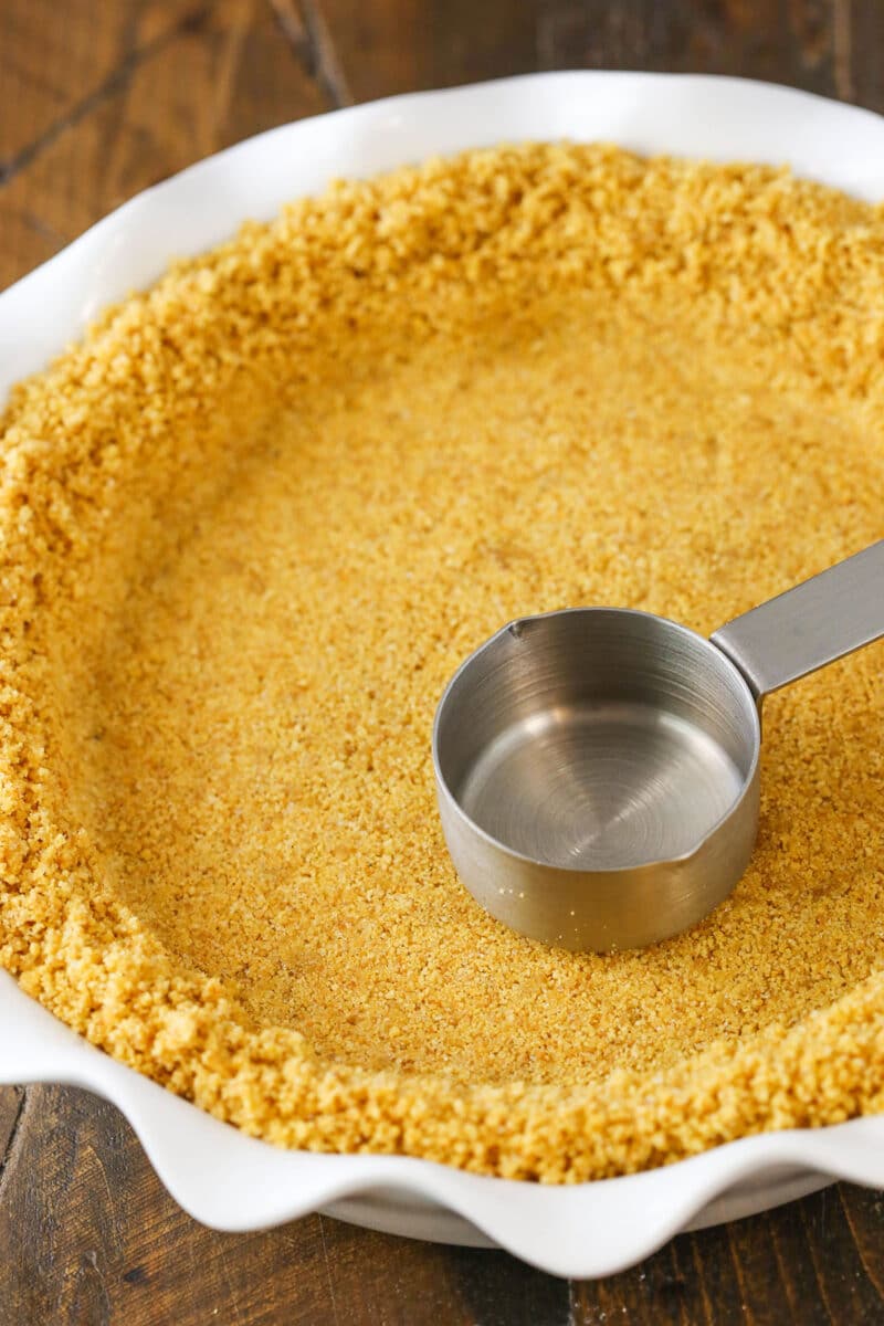 Using the bottom of a measuring cup to press graham cracker crumbs into a pie plate