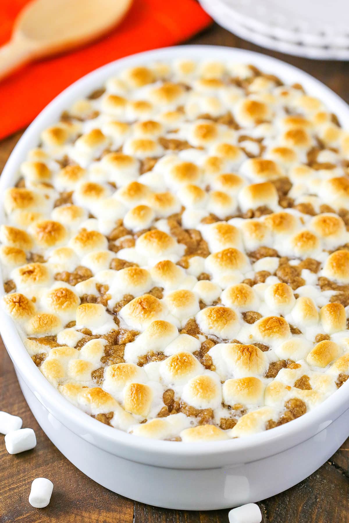 This easy Sweet Potato Casserole recipe is loaded with brown sugar, cinnamon and nutmeg and topped with toasty marshmallows and cinnamon streusel! Loaded Sweet Potatoes in a white oval casserole dish on a wooden table