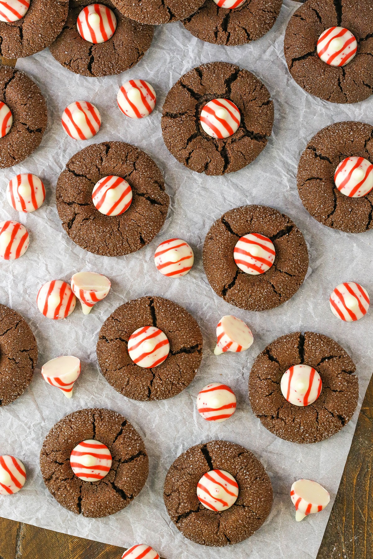Overhead view of Peppermint Chocolate Thumbprint Cookies spread evenly over parchment paper on a wooden table