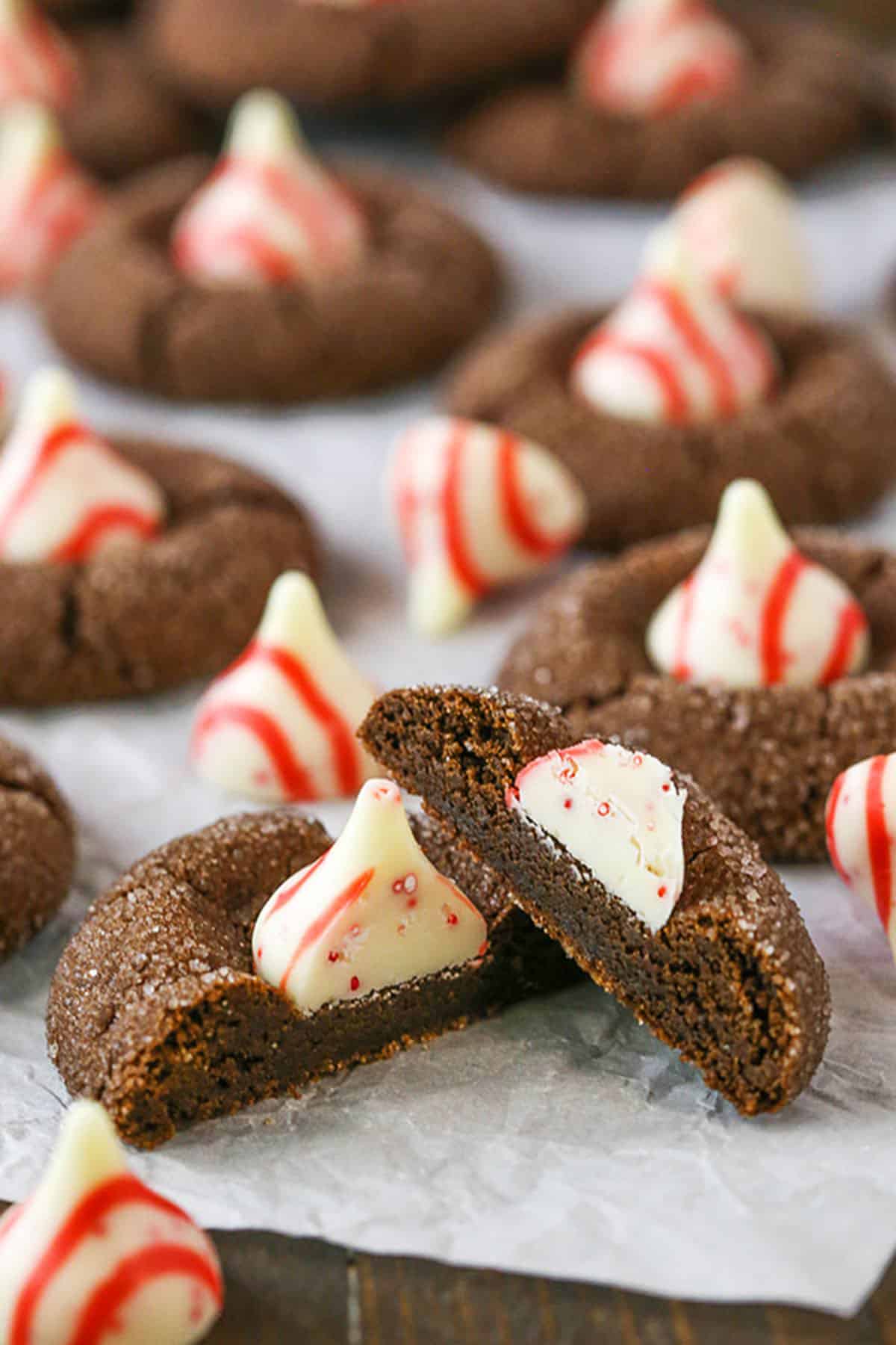A Peppermint Chocolate Thumbprint Cookie broken in half with whole Peppermint Chocolate Thumbprint Cookies in the background