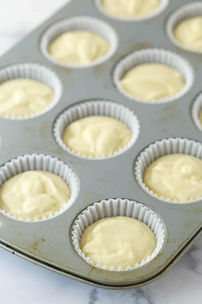 A cupcake pan full of cupcake liners filled with vanilla cupcakes batter.